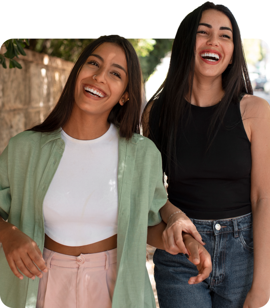 Two women laughing and holding hands while enjoying a walk outside on a sunny day.