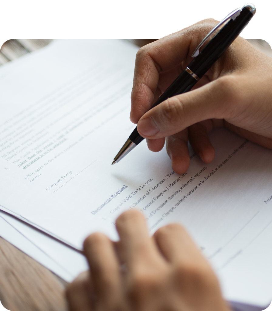 Person signing an important document with a black ink pen on a wooden table, close-up view of hand and paperwork.