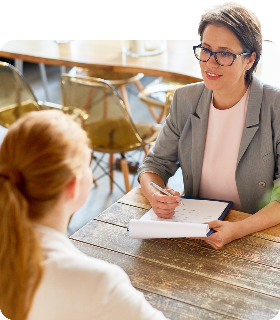 Woman in glasses conducting a job interview at modern office, holding a clipboard and pen, engaging in a discussion.