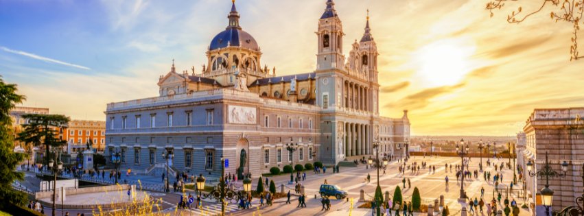 Almudena Cathedral in Madrid at sunset, with people walking around the historic square. Beautiful Spanish architecture.